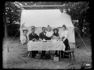 Six unidentified people sitting at a table having a cup of tea